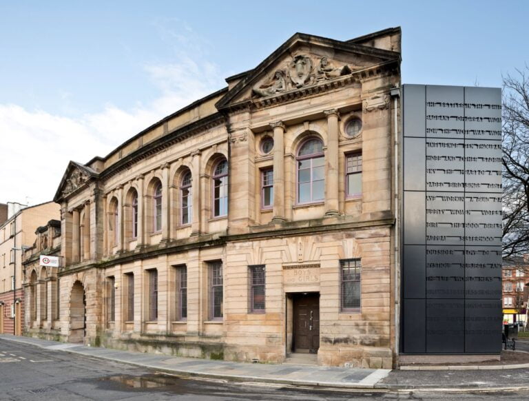Colour photo showing the exterior of Glasgow Women's Library and freestanding lift shaft. The building is blonde sandstone