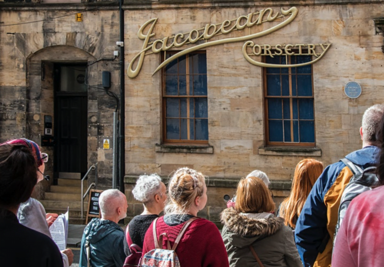 Ghost Signs of Glasgow walking tour with assembled group looking over to a gold wall sign of a business no longer there