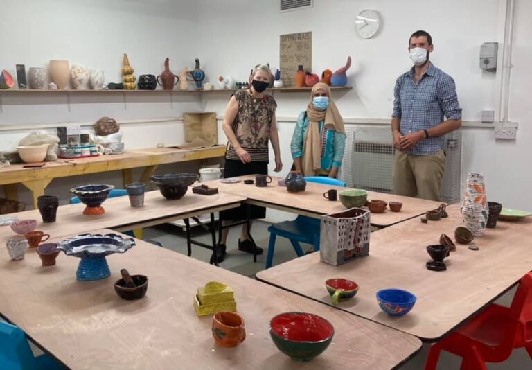 Three people standing in a room with a lot of ceramic objects arranged on tables and on shelves