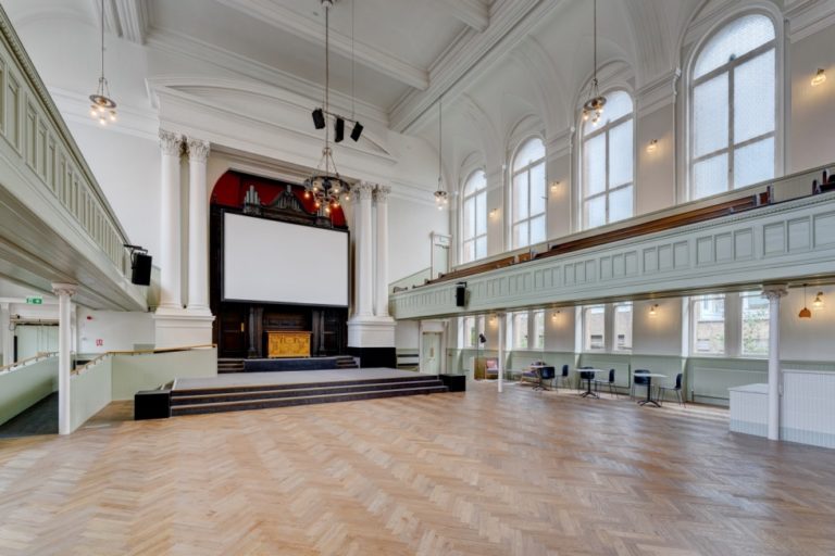 Interior of auditorium at Adelaide Place showing parquet flooring, ramped stage, projection screen and organ pipes.