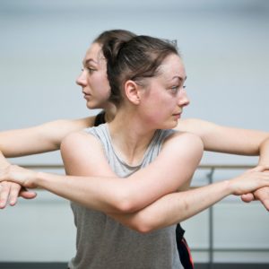 2 dancers stand infront and behind with arms interlaced.