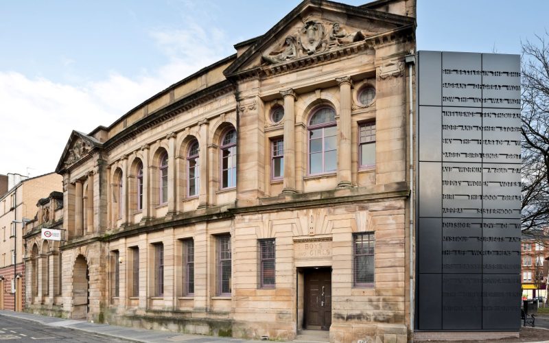 Colour photo showing the exterior of Glasgow Women's Library and freestanding lift shaft. The building is blonde sandstone
