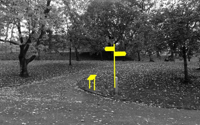 A black and white photograph of a paved path inside a park. It is the autumn and the trees are dropping their leaves. A wayfinding sign and map are blocked out in neon yellow.